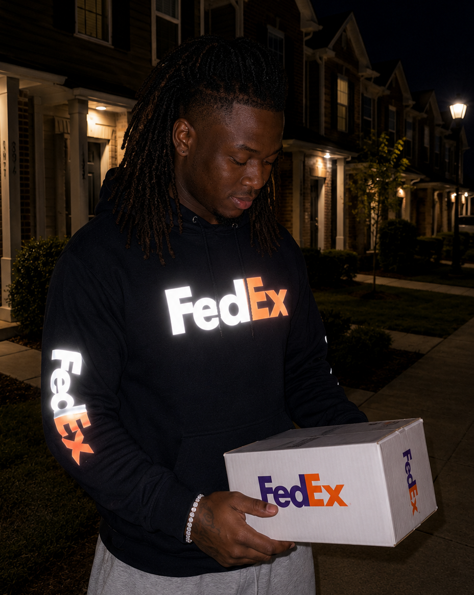 FedEx delivery driver wearing a reflective FedEx hoodie while delivering at night holding a FedEx package