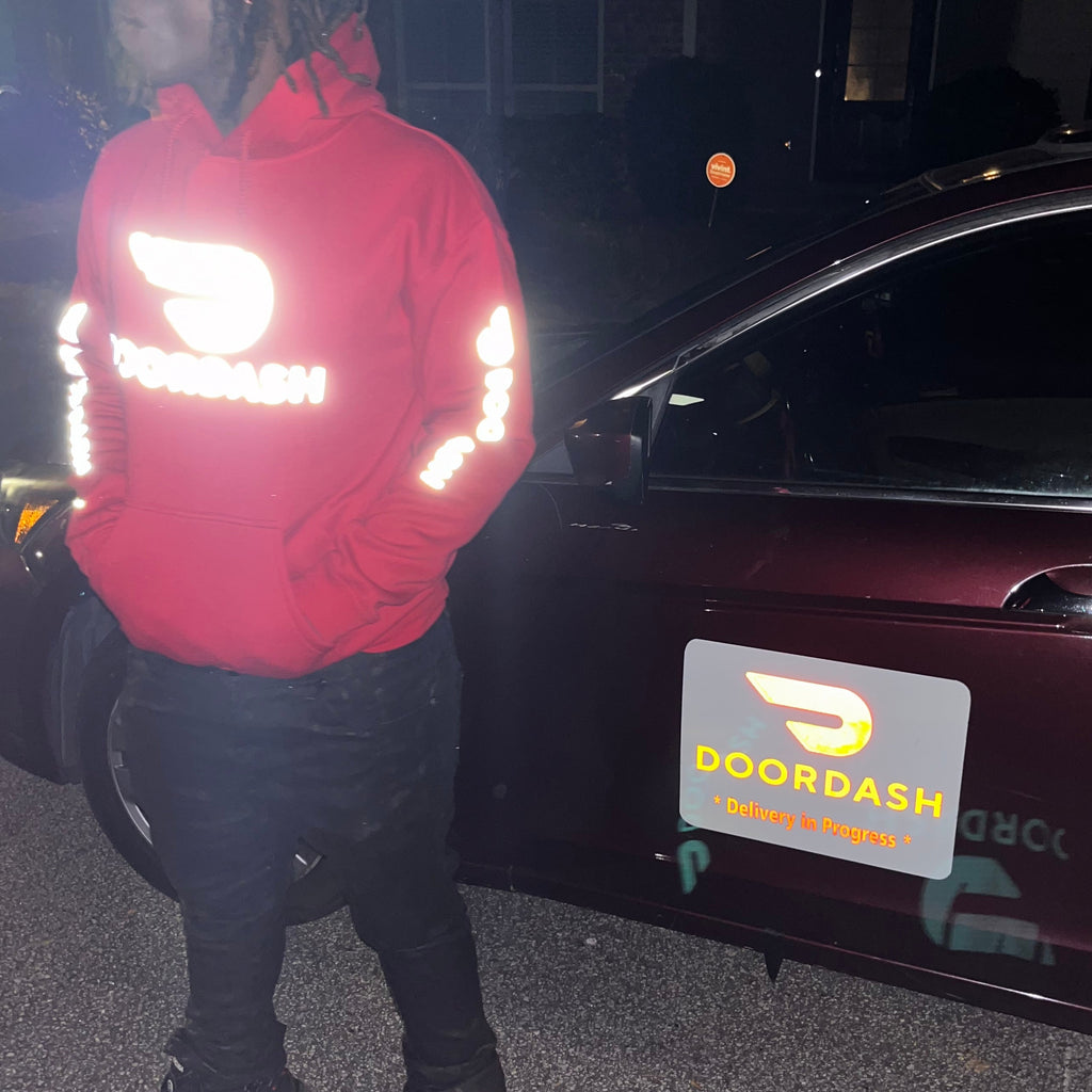 Person wearing a Reflective DoorDash red hoodie standing next to a car with a Reflective DoorDash Magnet