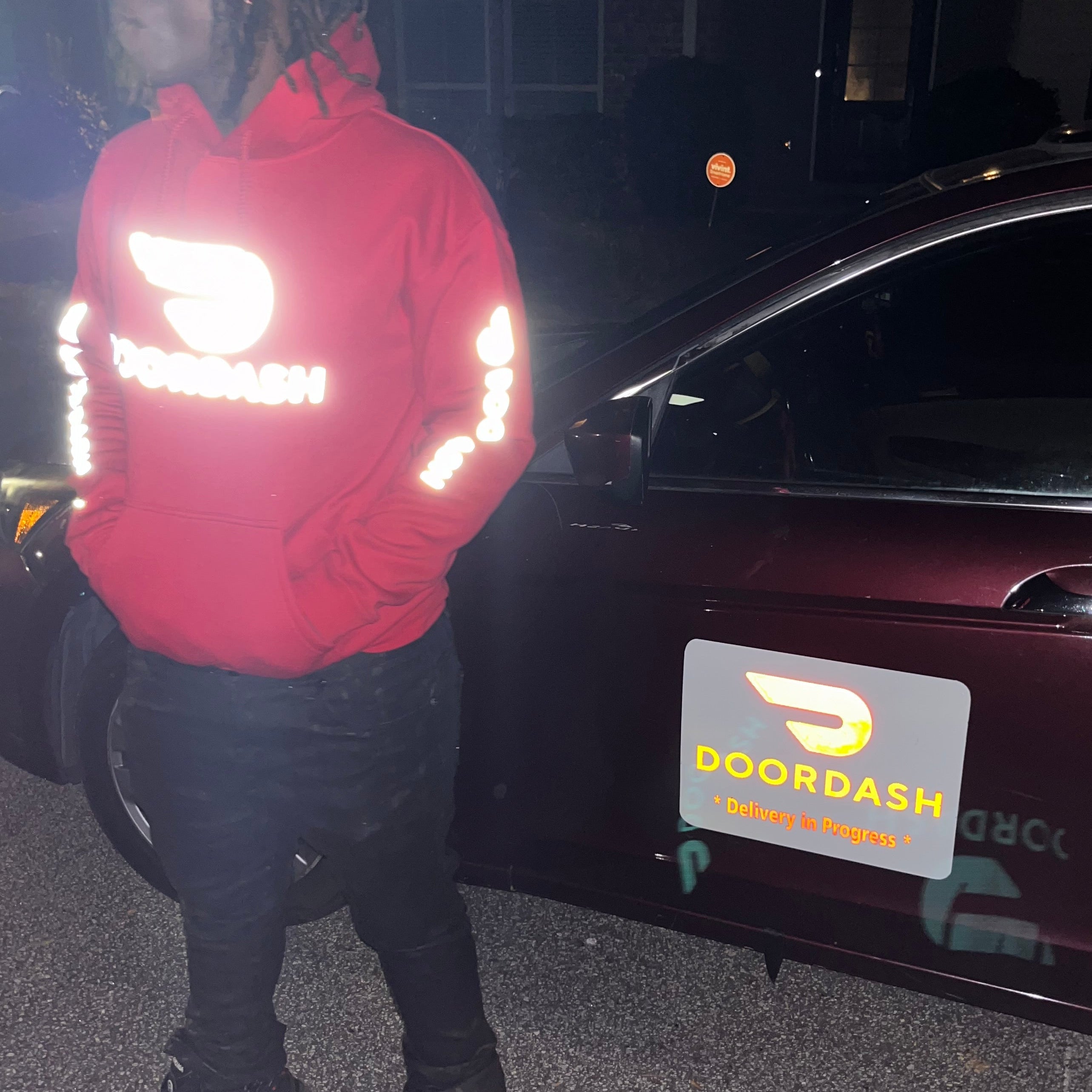 Person wearing a Reflective DoorDash red hoodie standing next to a car with a Reflective DoorDash Magnet